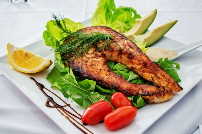 Grilled salmon fillet garnished with vegetables, lemon wedges, and sauce